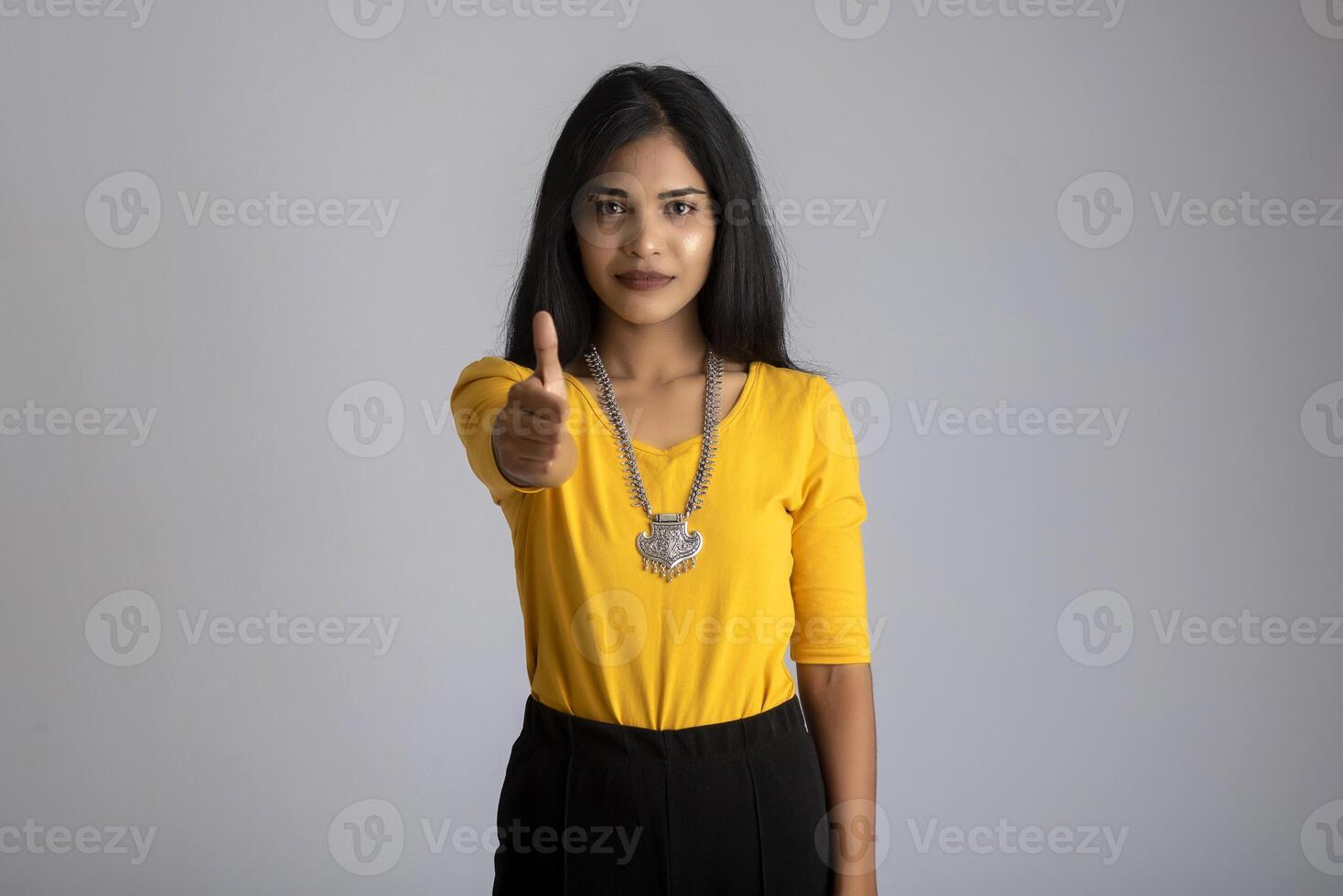 Young smiling girl showing ok sign or thumbs up on a grey background photo