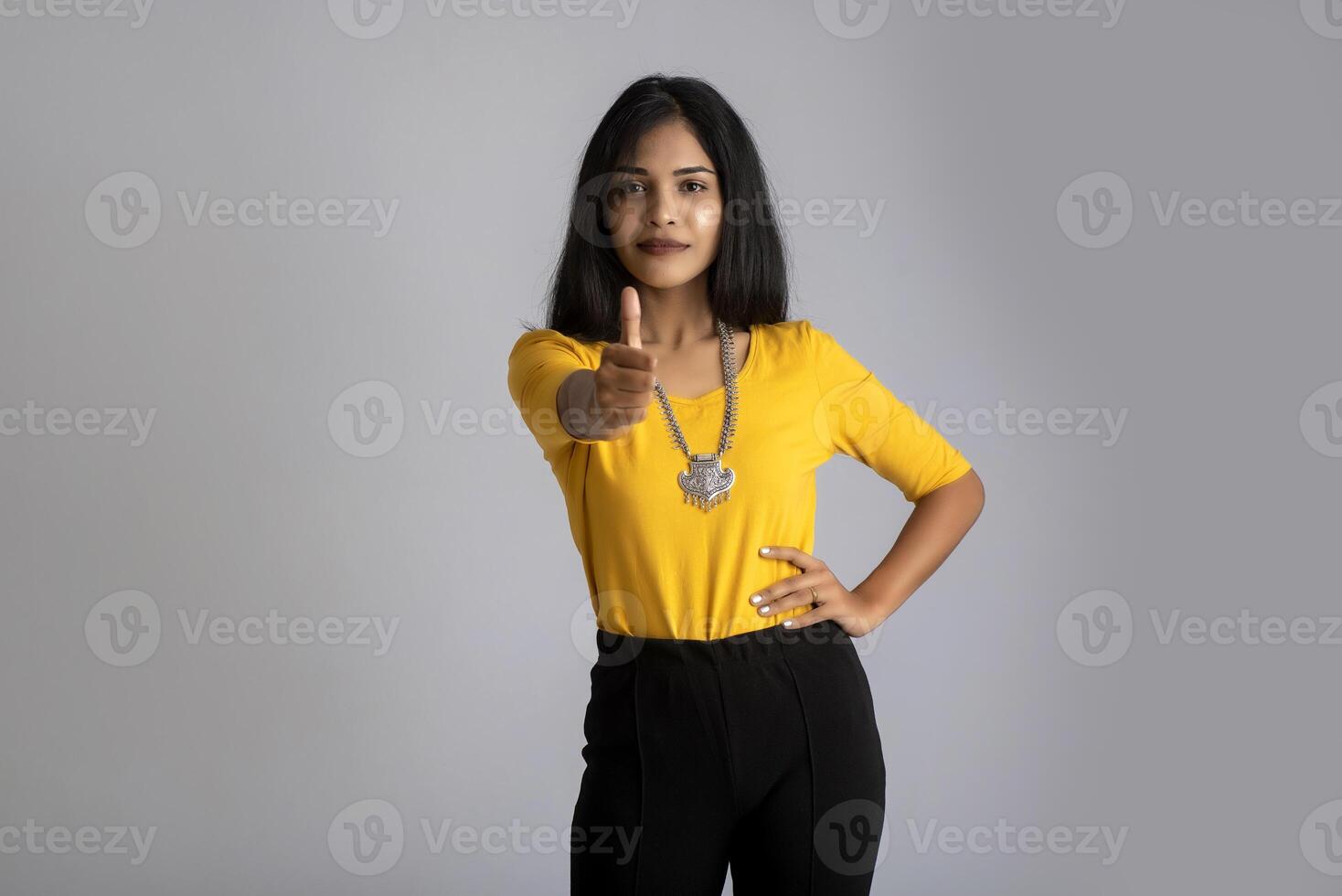 Young smiling girl showing ok sign or thumbs up on a grey background photo