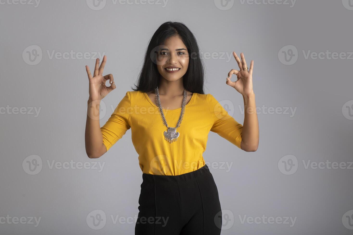 Young smiling girl showing ok sign or thumbs up on a grey background photo