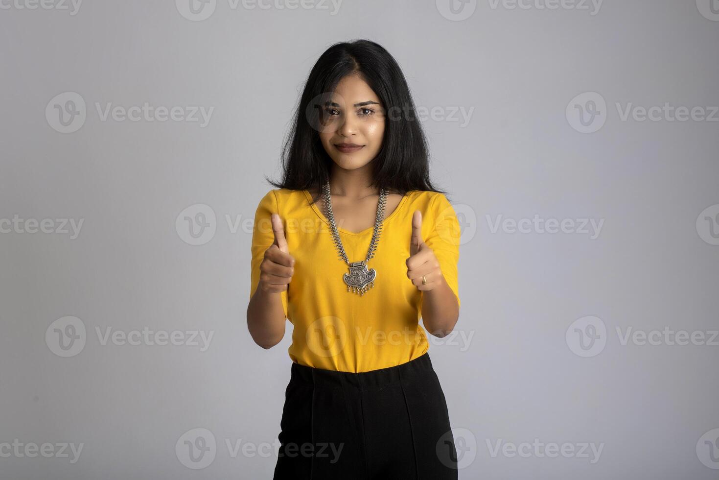 Young smiling girl showing ok sign or thumbs up on a grey background photo