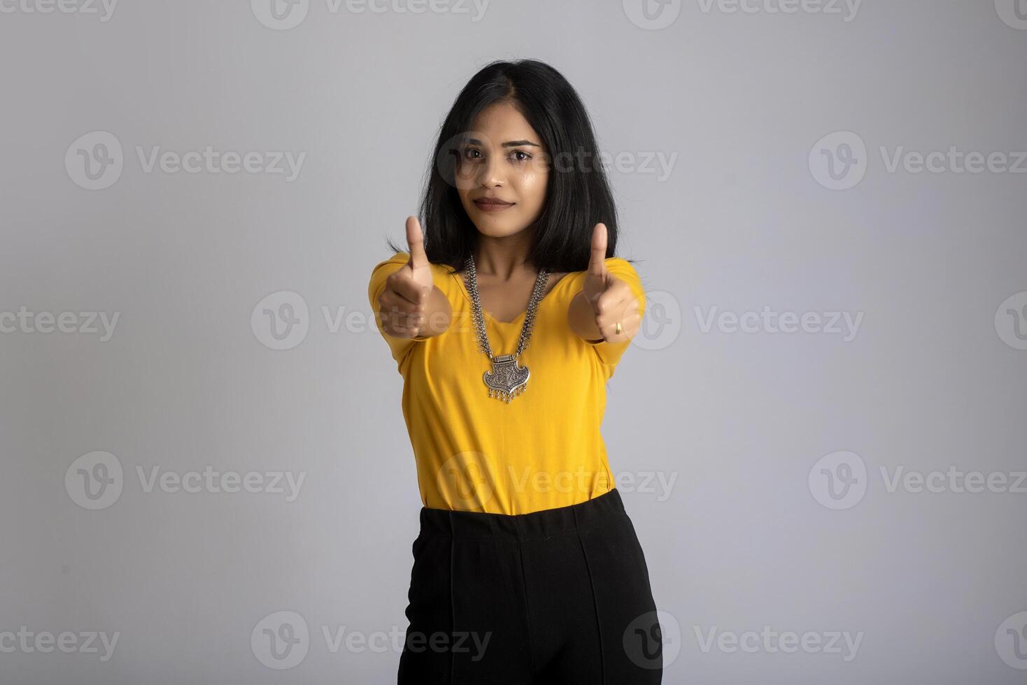 Young smiling girl showing ok sign or thumbs up on a grey background photo
