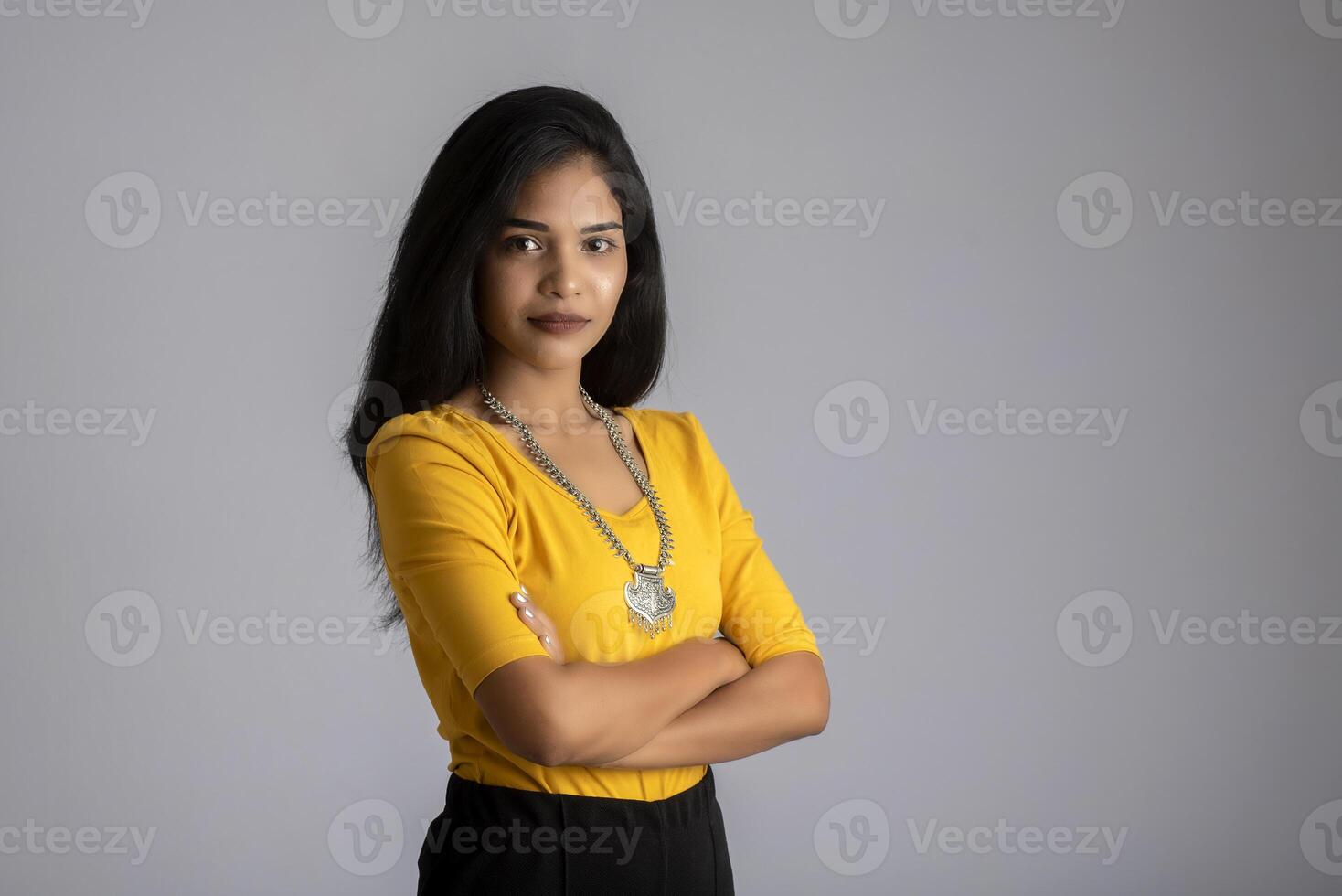 Portrait of a beautiful, smiling, emotional young woman posing with hands-folded on gray background. photo
