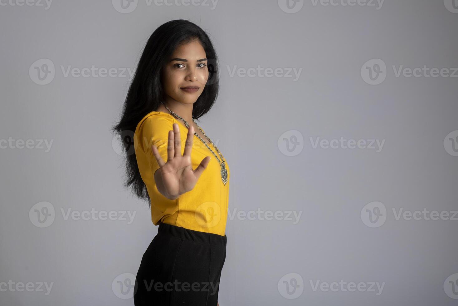 Portrait of a beautiful girl showing stop sign with palms on a grey background photo