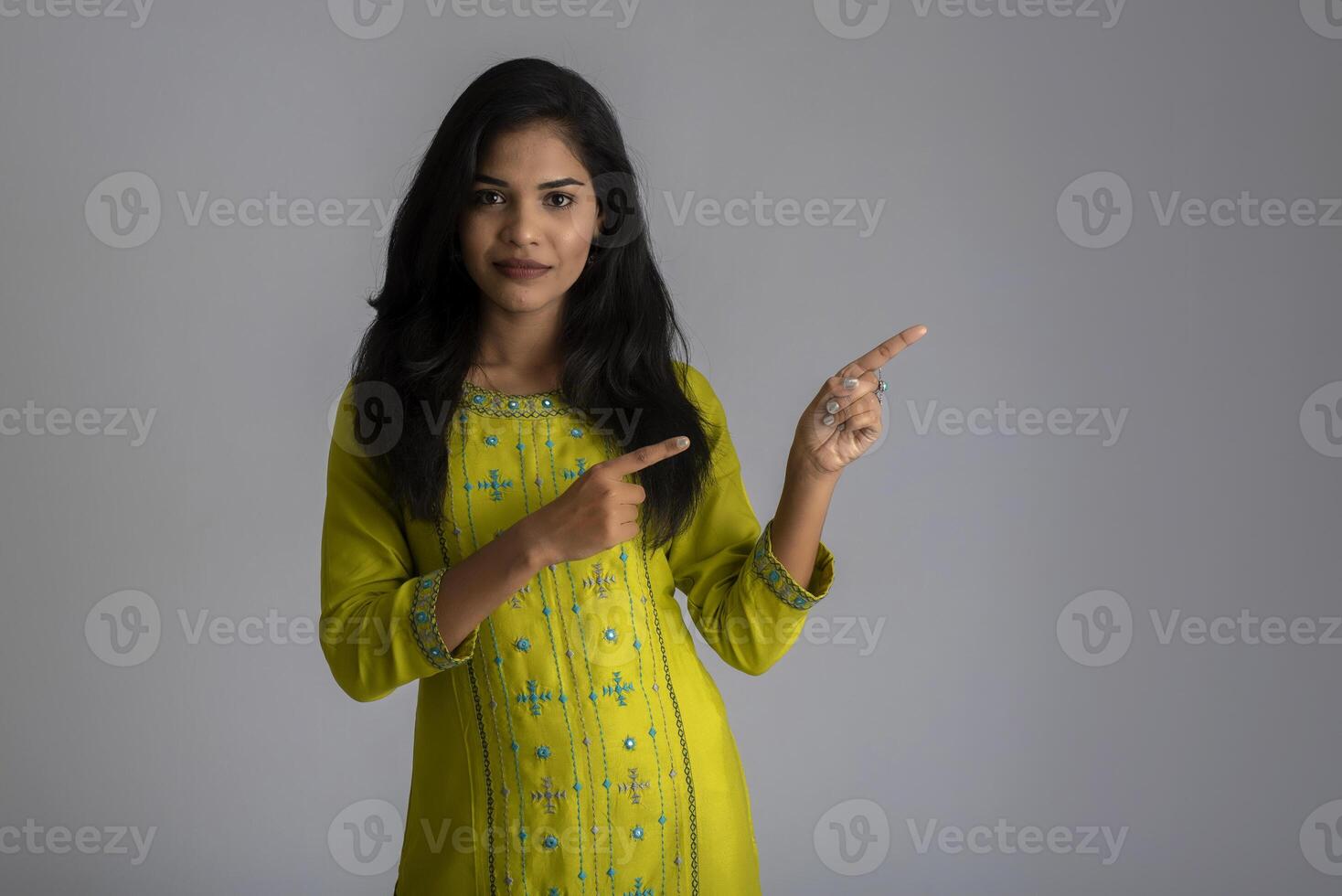 Portrait of a successful cheerful young girl holding and presenting something on hand with a happy smiling face. photo