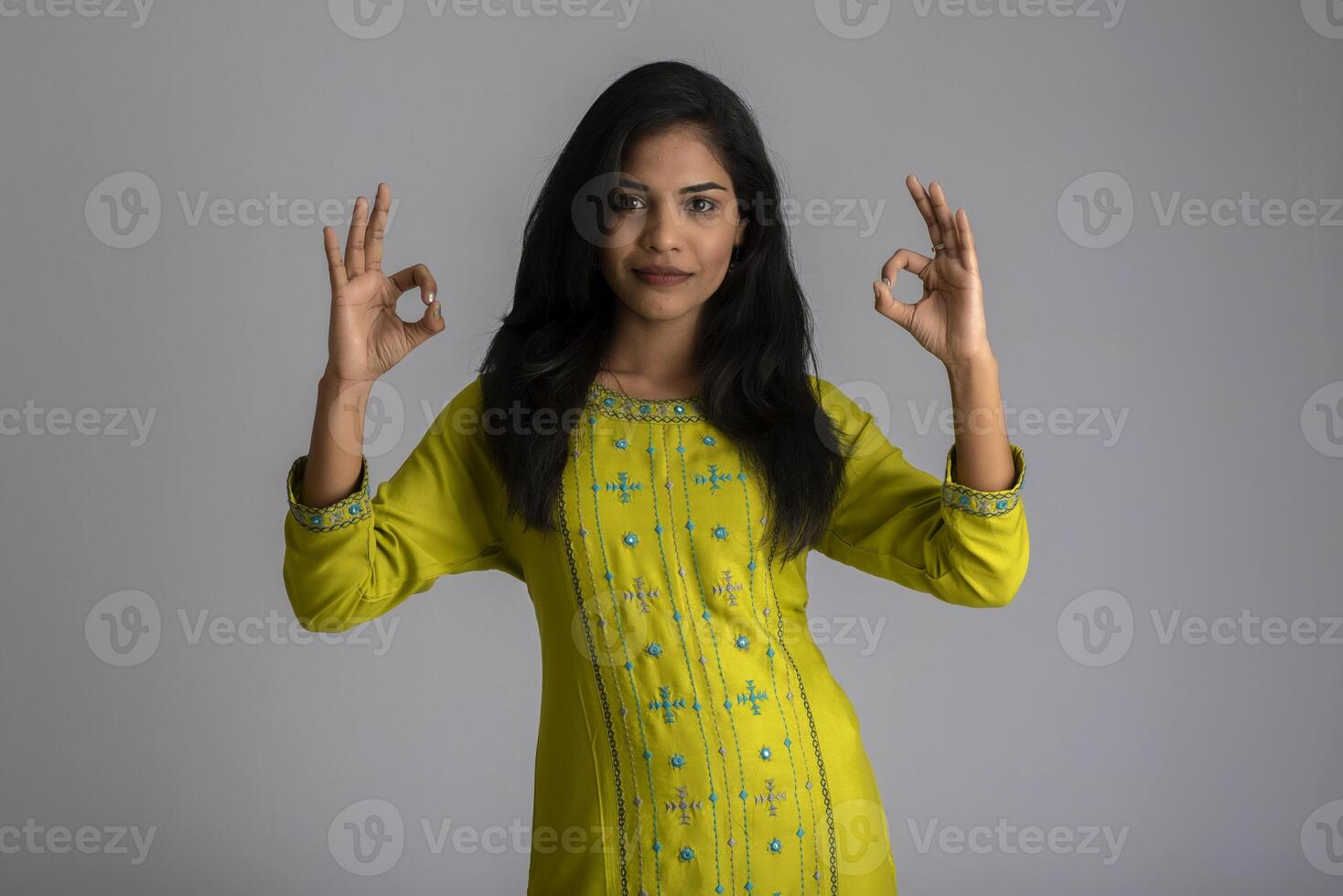 Young smiling girl showing ok sign or thumbs up on a grey background photo