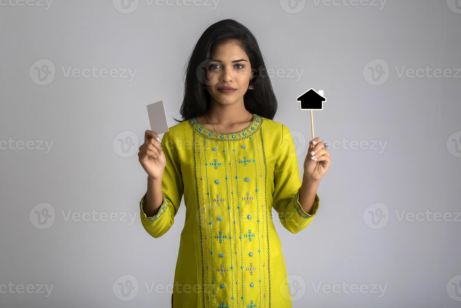 Young smiling beautiful girl showing a credit card or blank card with a black board on grey background. photo