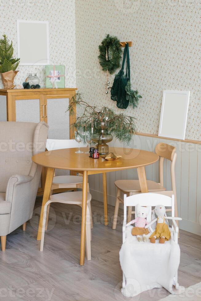Christmas decor in the living room in the Scandinavian style, two glasses on a wooden table, spruce branches in a vase and candles, a high chair with toys photo