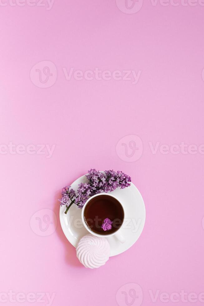Flower arrangements of beautiful purple lilac on a pink background with a cup of tea. Women's office desk, stylish stock image, Flat layout, top view with Empty copy space photo