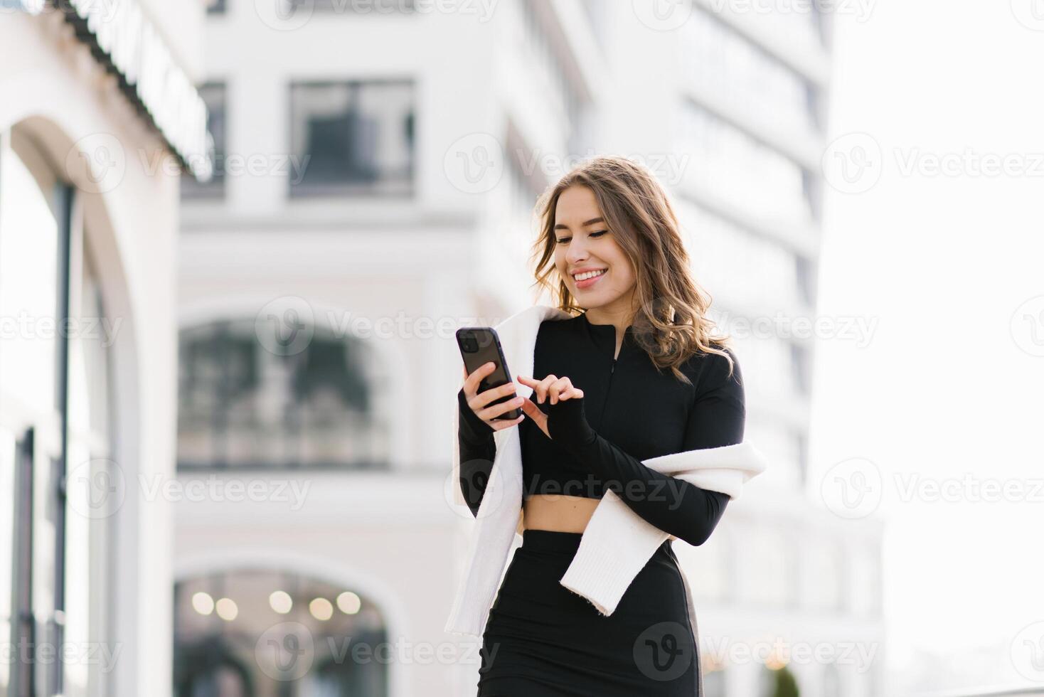 Young woman holds a smartphone in her hands and makes purchases online or communicates in a social network while walking through the streets of the city photo