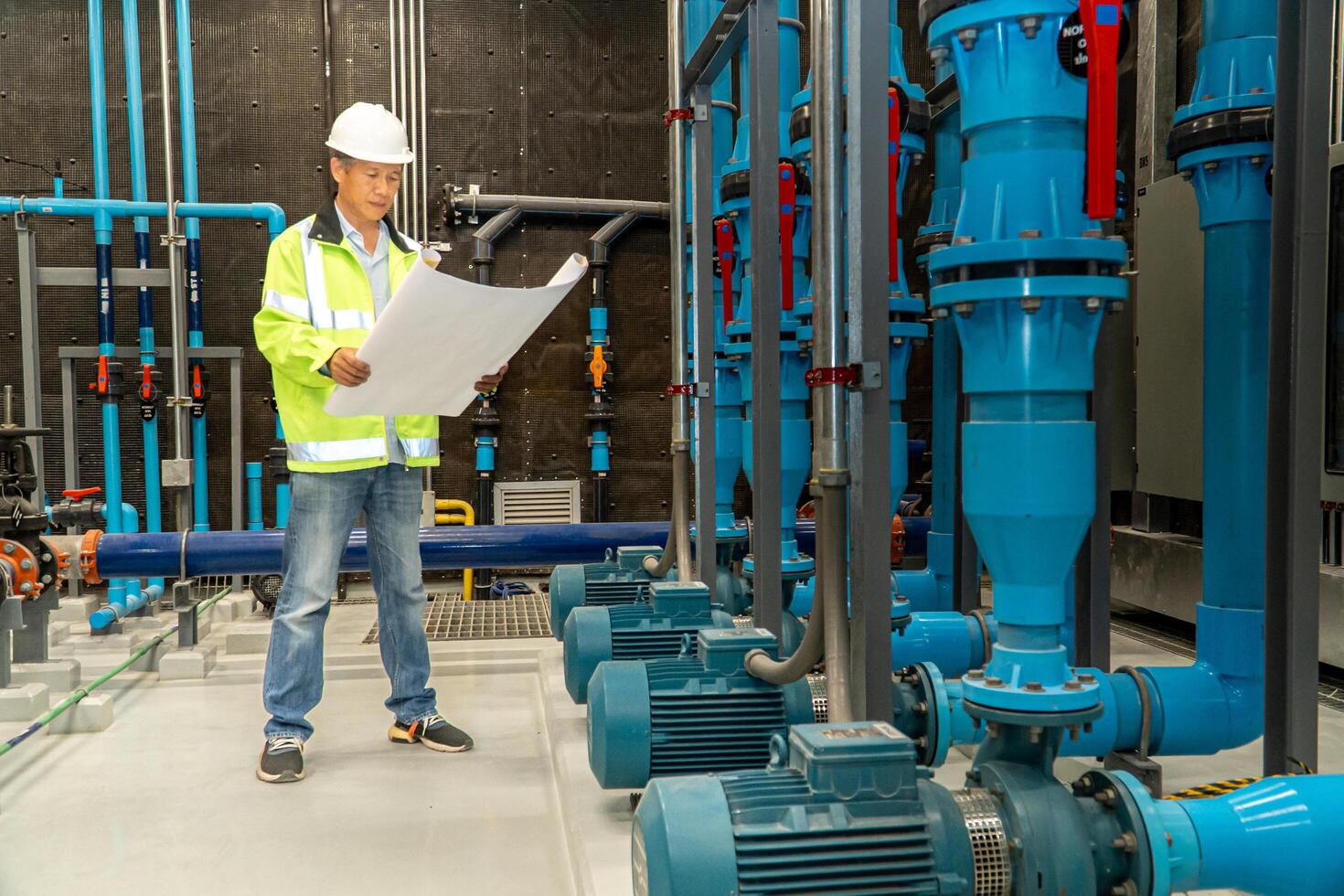 asian man worker in protective uniform and with hardhat using tablet for checking temperature in pipes Factory interior. photo