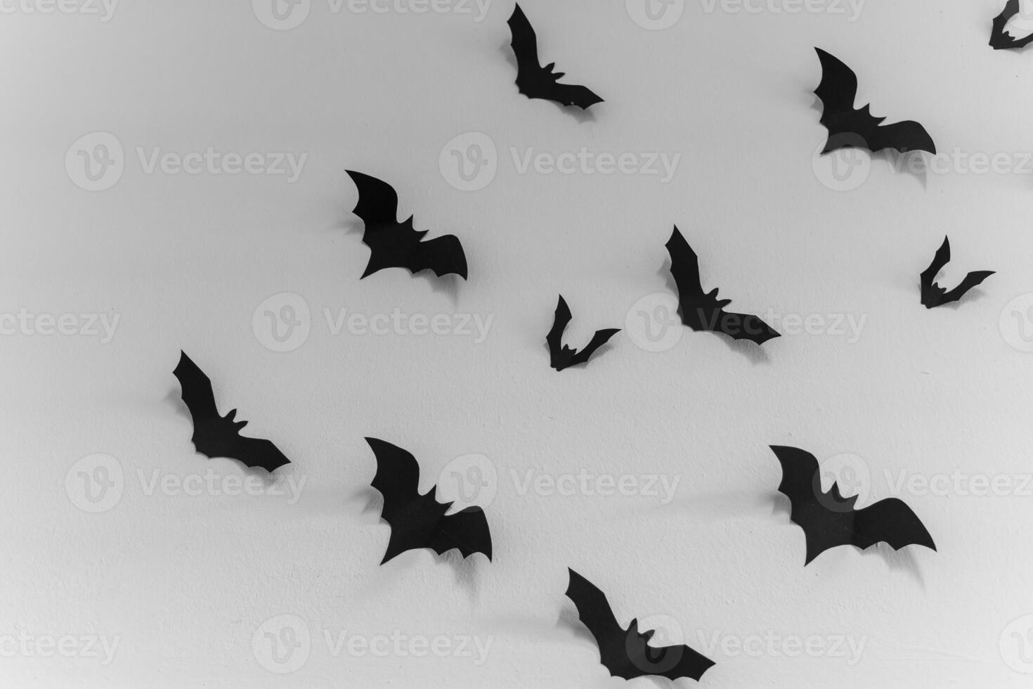 Black paper bats are scattered across a white wall, creating a spooky and whimsical Halloween decoration photo