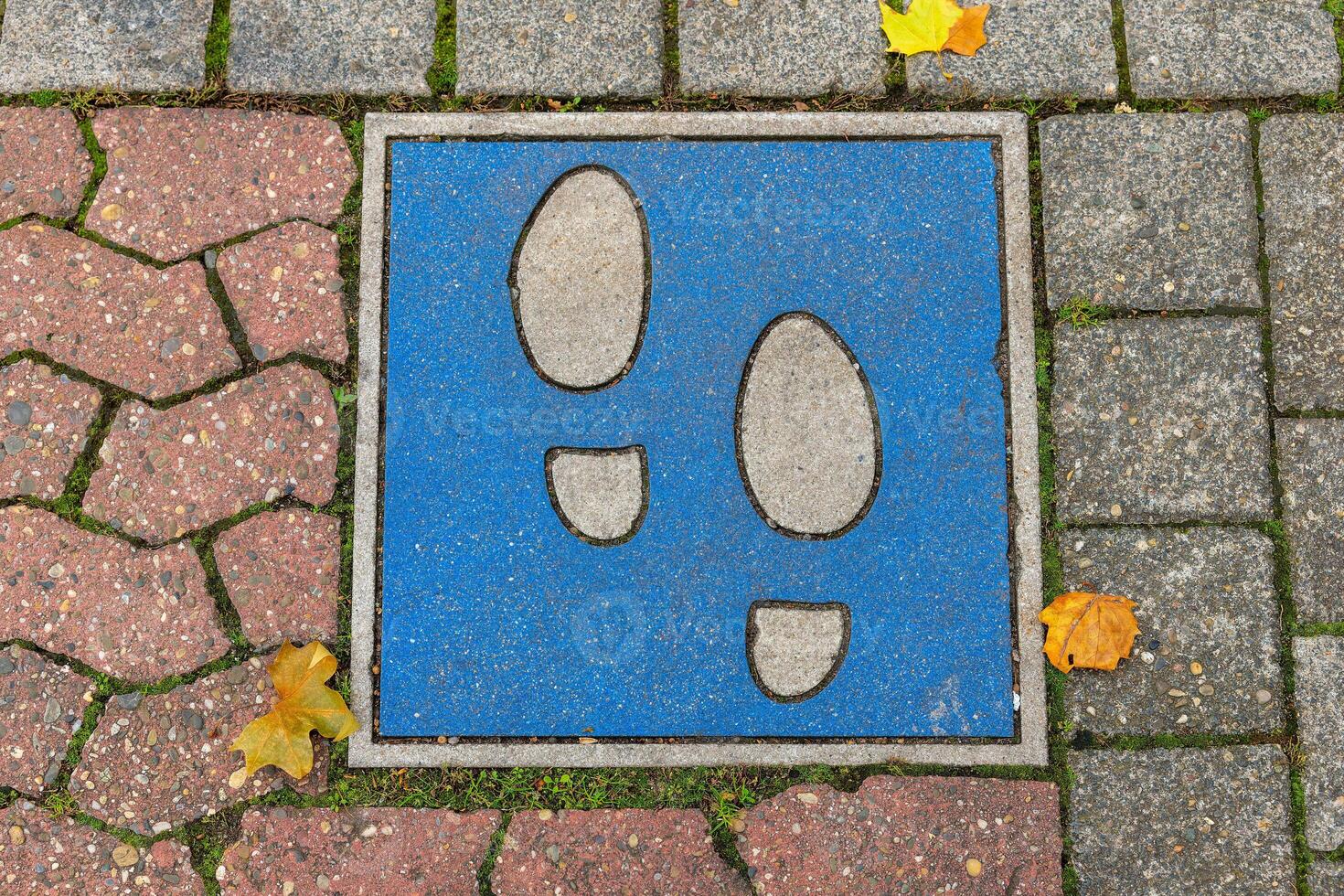 blue sign with two black feet on it is on a brick sidewalk. The sign is placed on a section of the sidewalk that is made of red and white bricks photo