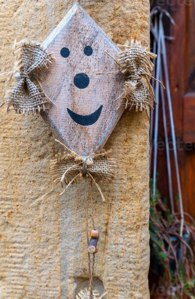 A wooden sign with a smiling face is hanging on a stone wall in a quaint village photo