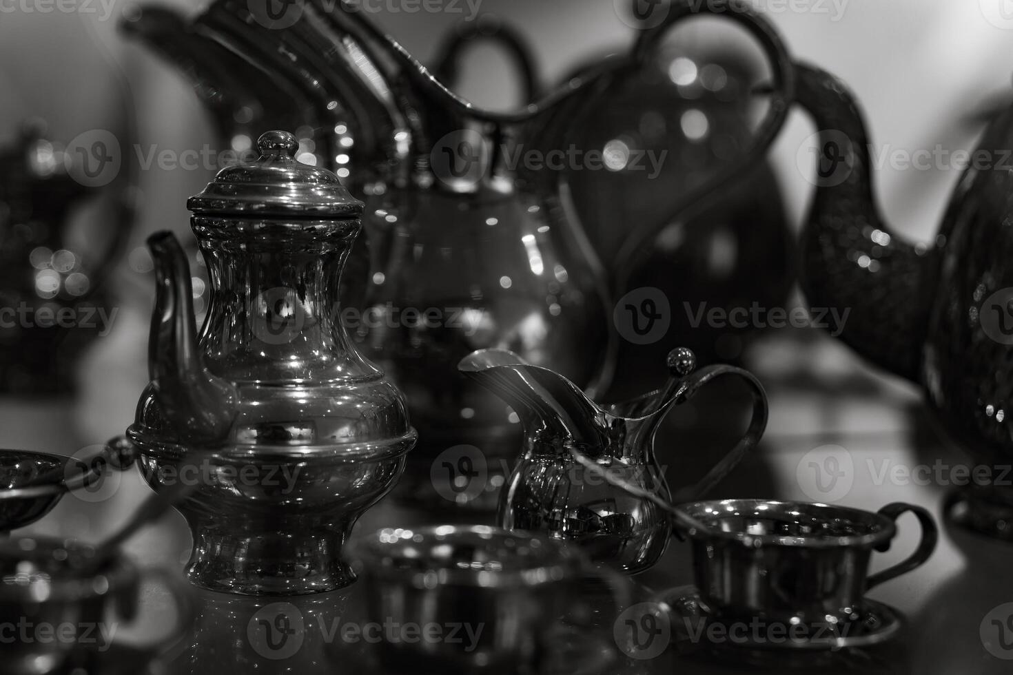 A collection of silver teapots and cups are displayed on a table photo