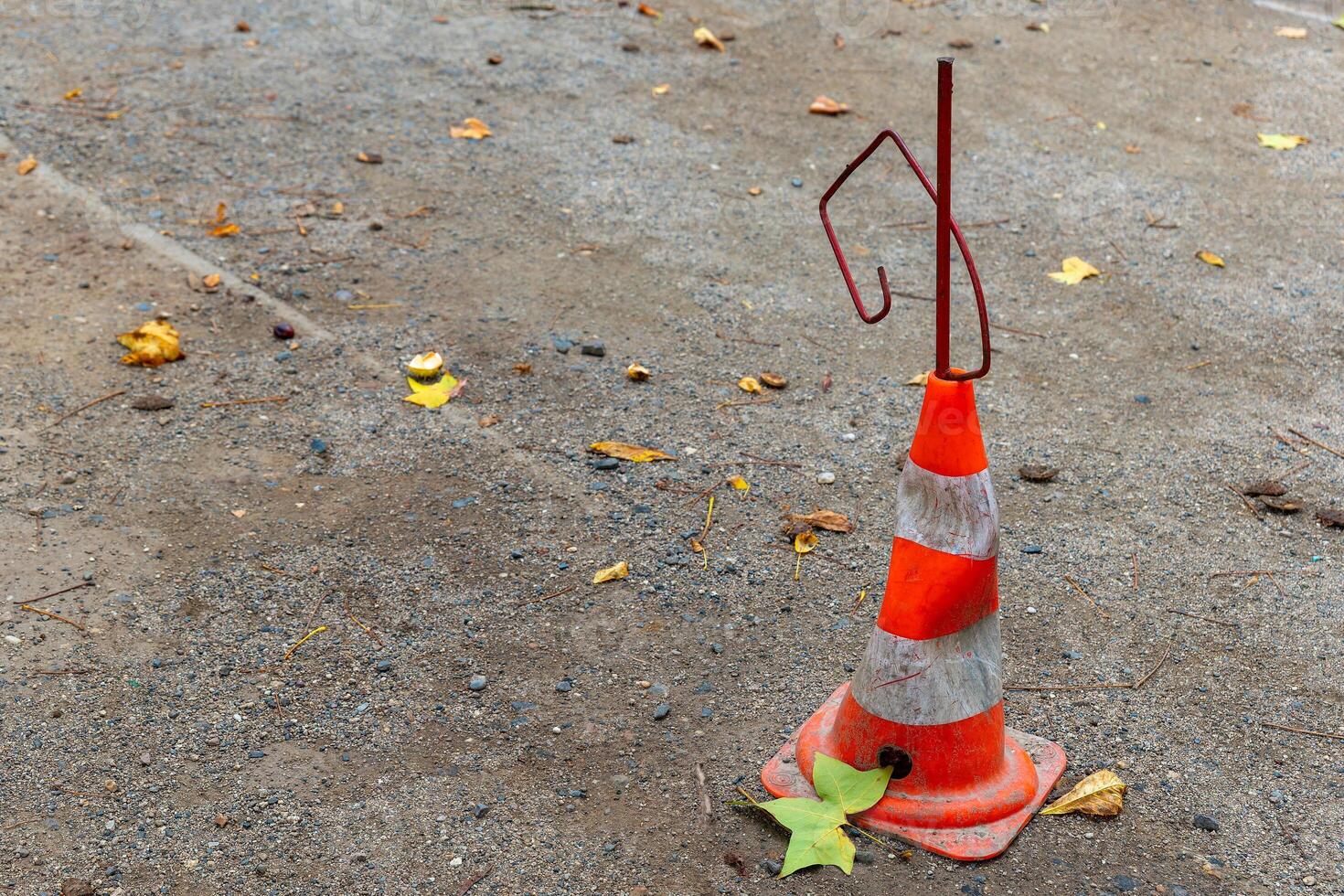 A traffic cone sits on a gravel road with some fallen leaves around it photo