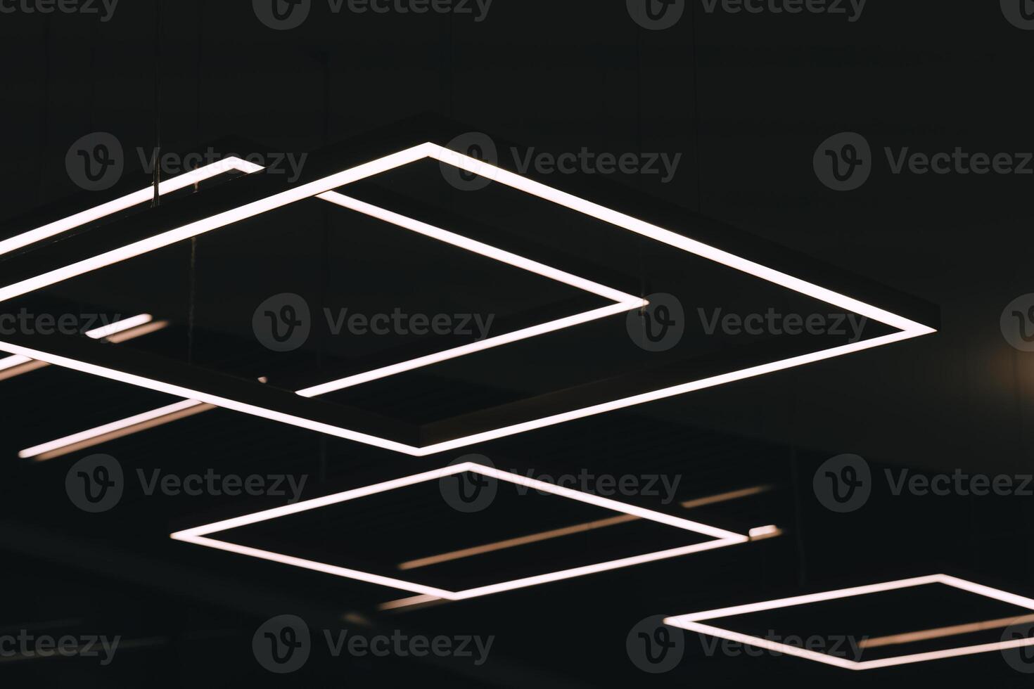 Geometric light fixtures illuminate the ceiling of a modern building photo