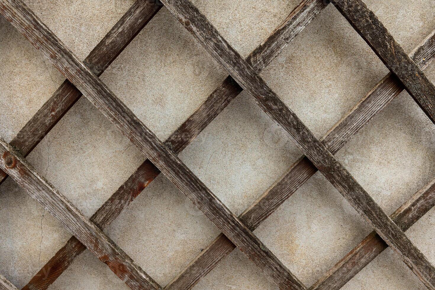 A close-up view of a weathered wooden trellis, showcasing its intricate diamond pattern against a textured background photo