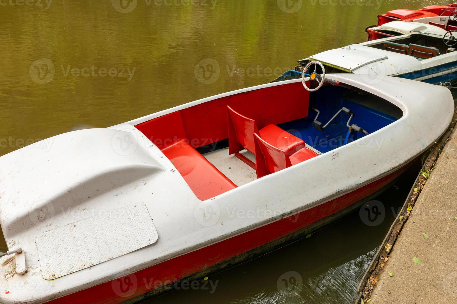 small red and white boat is sitting in the water. The boat is parked next to a dock photo