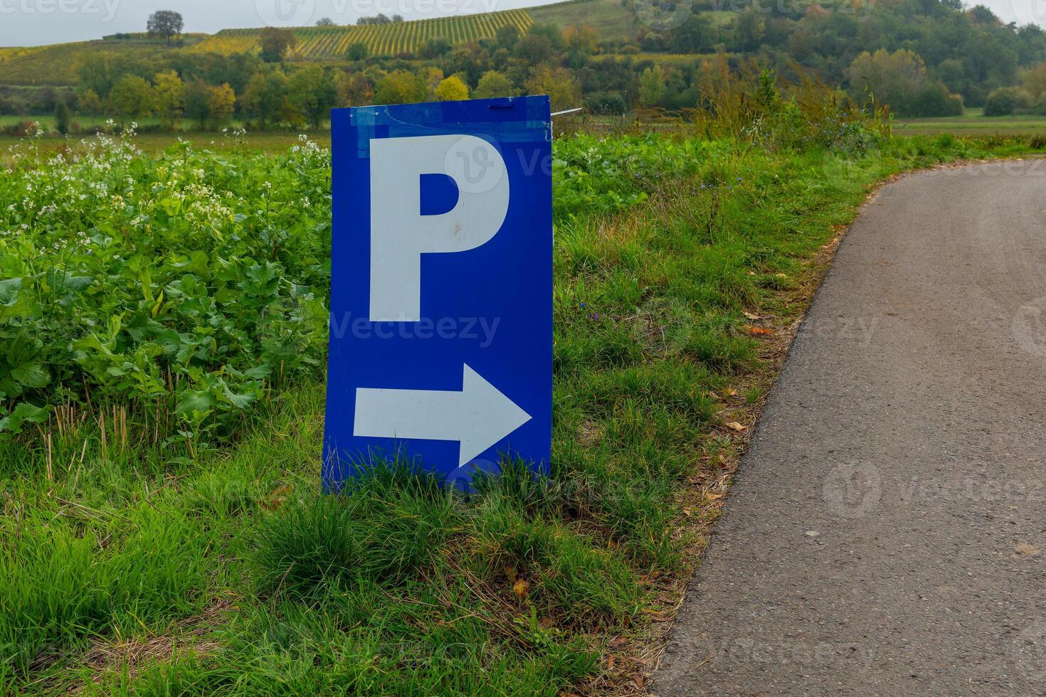 A blue parking sign with a white arrow pointing to the right sits on the side of a paved road photo