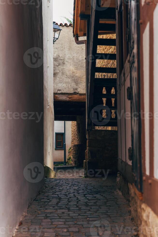 A narrow cobblestone alleyway winds through an old European city, lined with ancient buildings photo