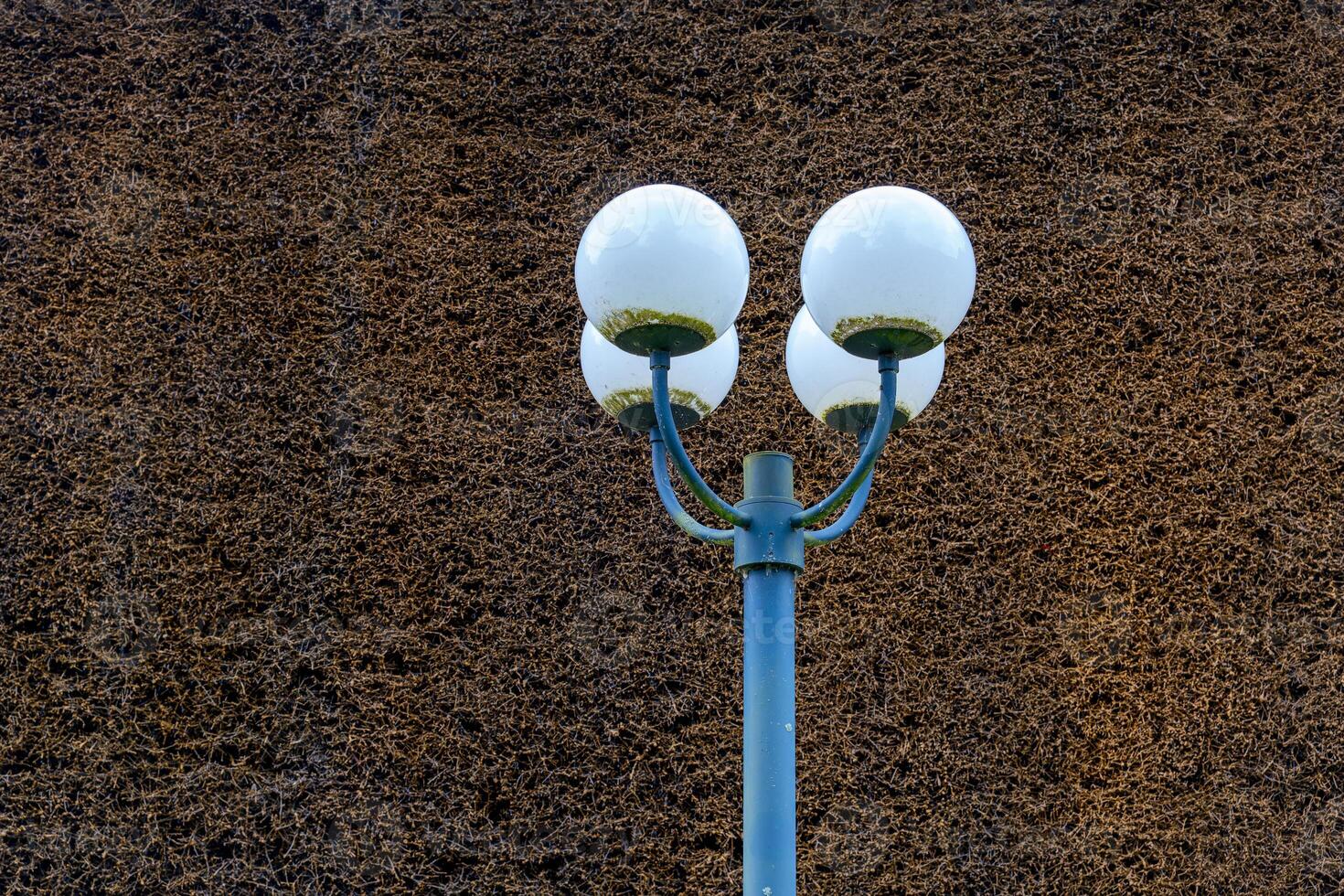 street light with three white globes is lit up against a dark background. The light is shining on a wall, creating a moody atmosphere photo