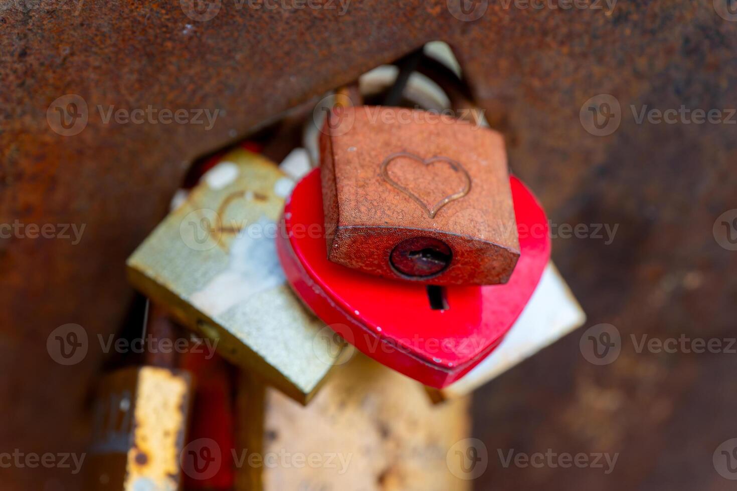 red heart is attached to a rusty lock. The lock is attached to a metal surface photo
