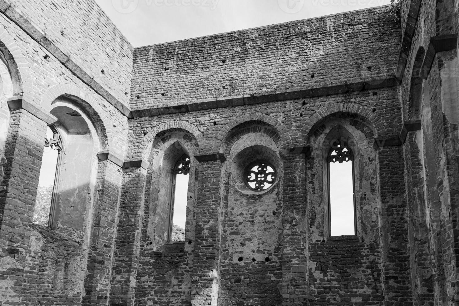 A view of the interior of a ruined building in Ireland, with windows and arches framing a view of the sky photo