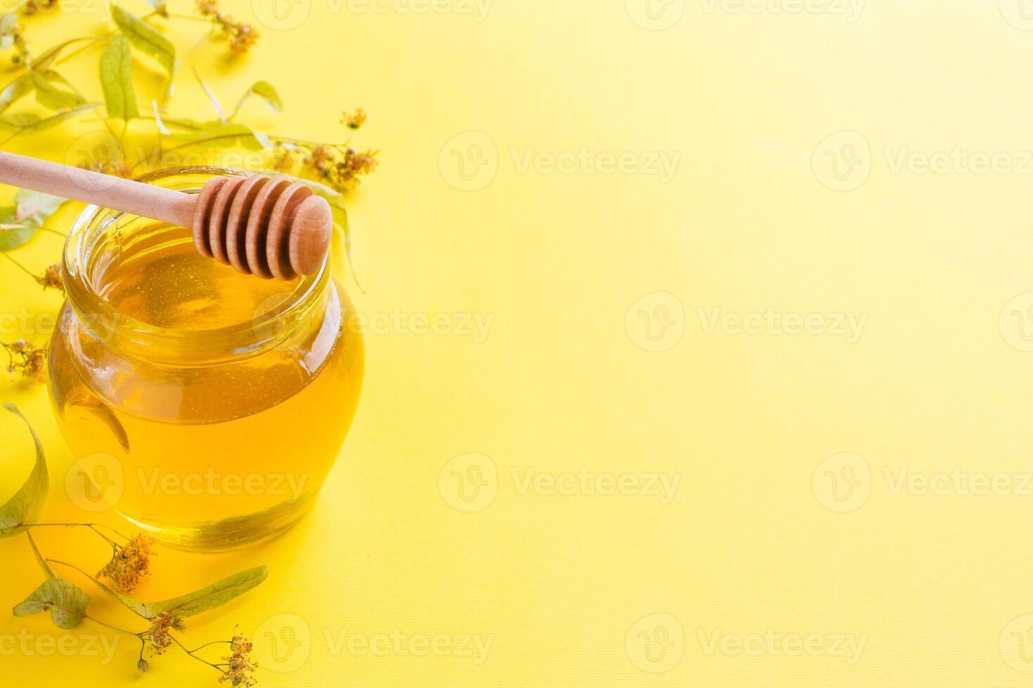 A jar of liquid honey from Linden flowers and a stick with honey on yellow background. Copy space photo