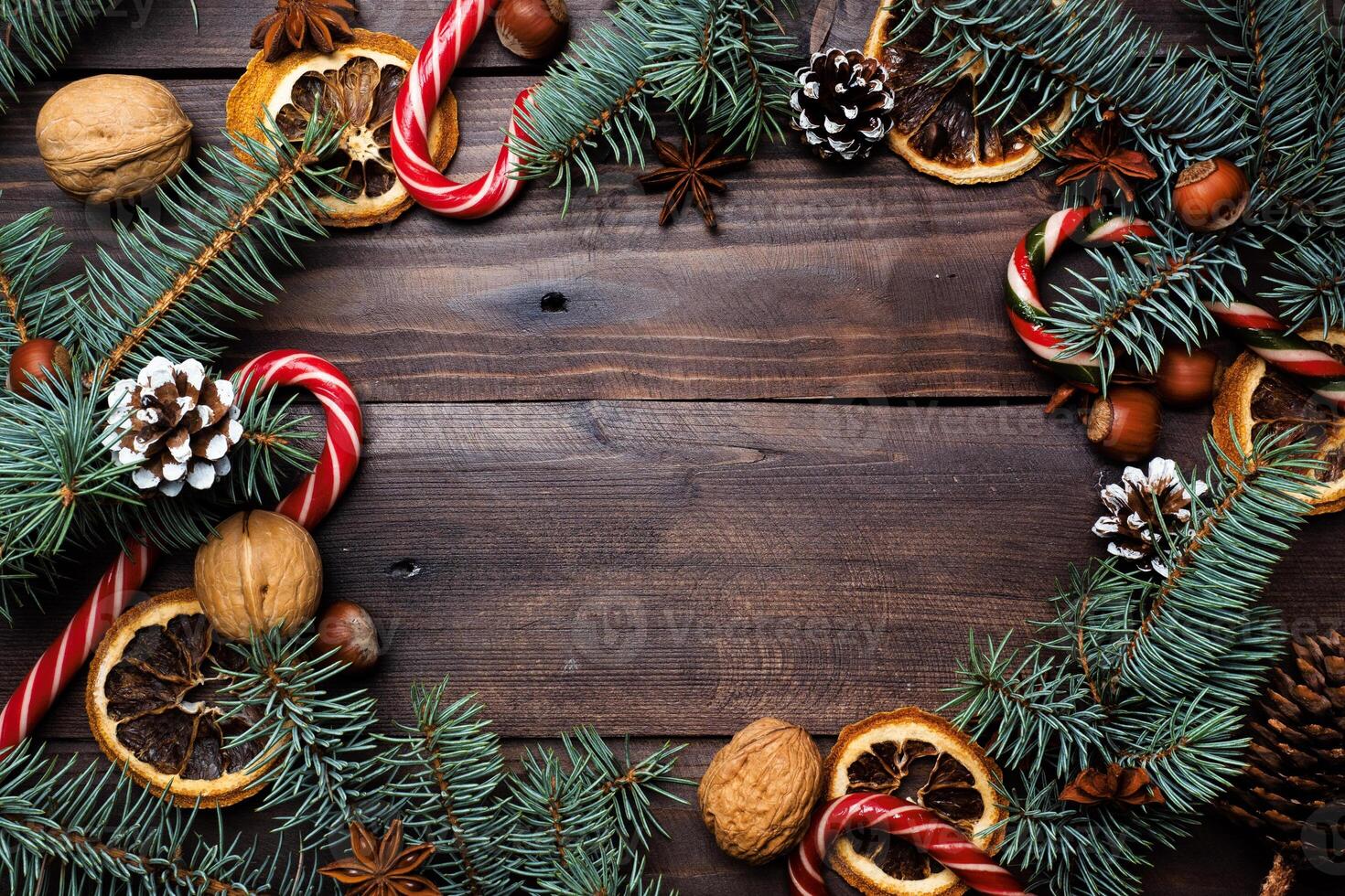 Frame of Christmas tree cones oranges caramel cane nuts on dark wooden background. Copy space. Flat lay. photo