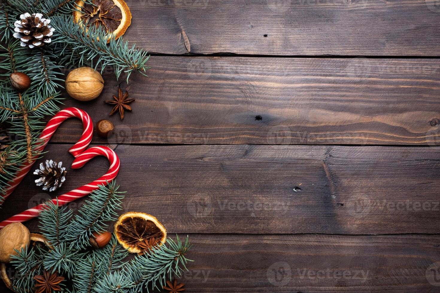 Frame of Christmas tree cones oranges caramel cane nuts on dark wooden background. Copy space. Flat lay. photo