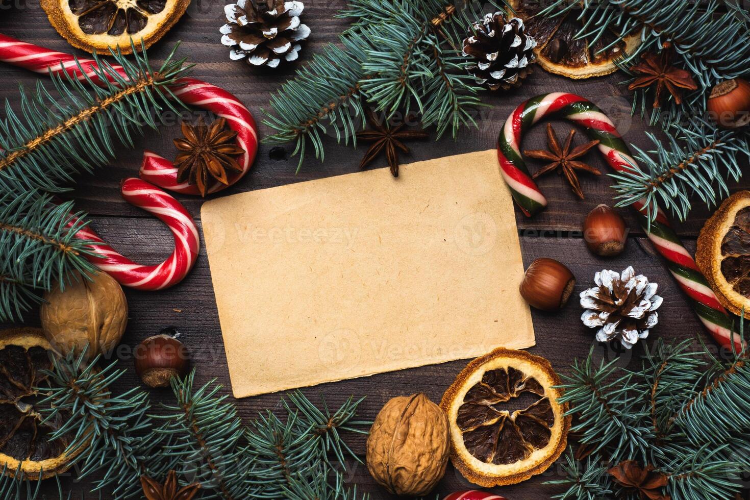 Frame of Christmas tree cones oranges caramel cane nuts on dark wooden background. Copy space. Flat lay. Old paper for text. photo