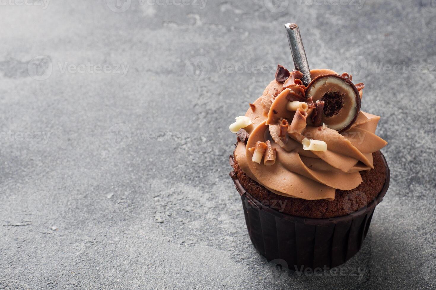 Chocolate muffin with cream decorated with candy and chocolate chips. Dark concrete background. Copy space. photo