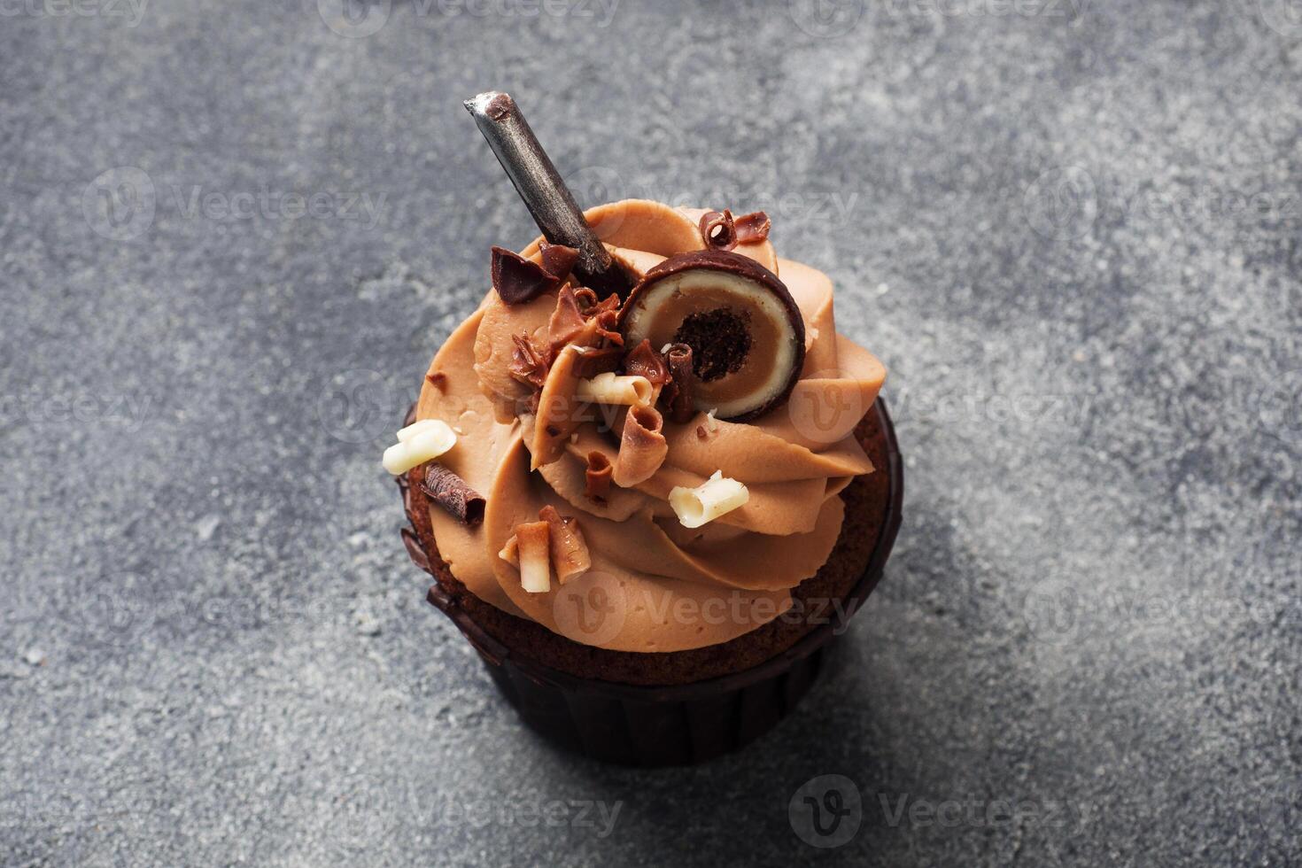 Chocolate muffin with cream decorated with candy and chocolate chips. Dark concrete background. Copy space. photo