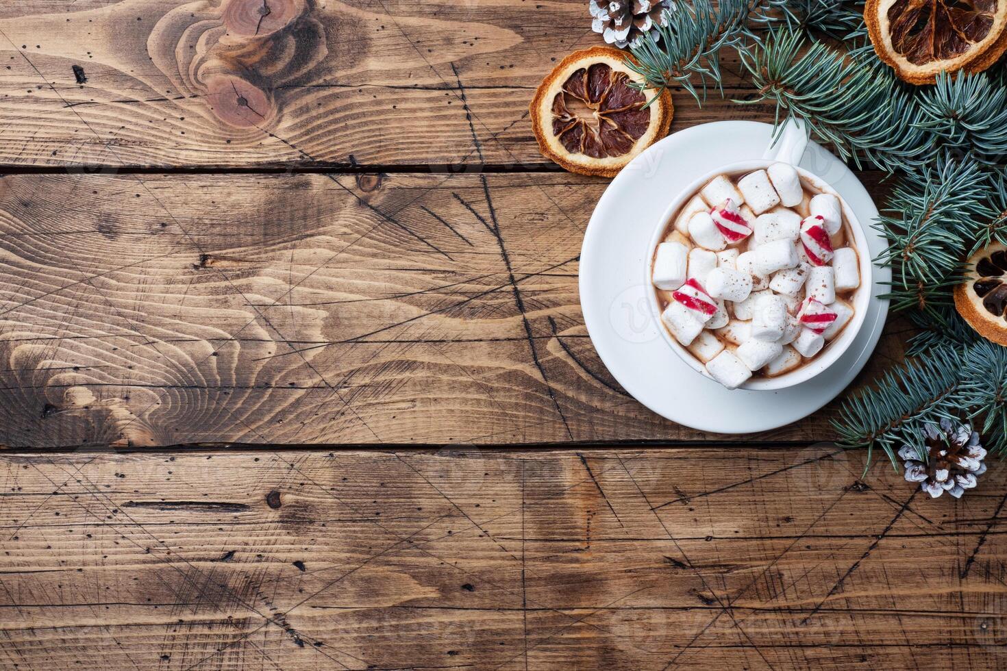 A Cup of hot chocolate with marshmallows. Christmas tree and decorations, cane caramel and oranges nuts Wooden background copy space. photo