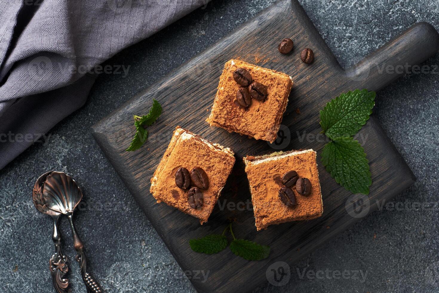 Pieces of tiramisu cake with delicate cream, coffee beans and mint leaves. Dark concrete background with copy space. Top view. photo