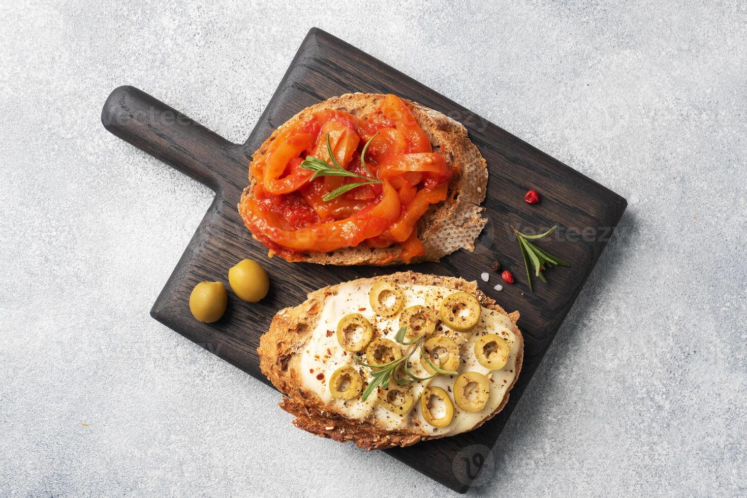 Whole grain bread sandwiches with cream cheese, olives and canned peppers with tomato on a wooden cutting Board. Gray concrete background with Copy space. photo