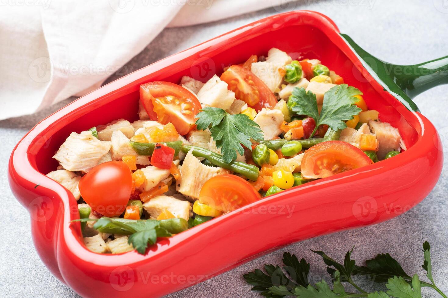 Stewed chicken meat with vegetables carrots peppers peas corn in a plate in the form of red pepper. Copy space. photo