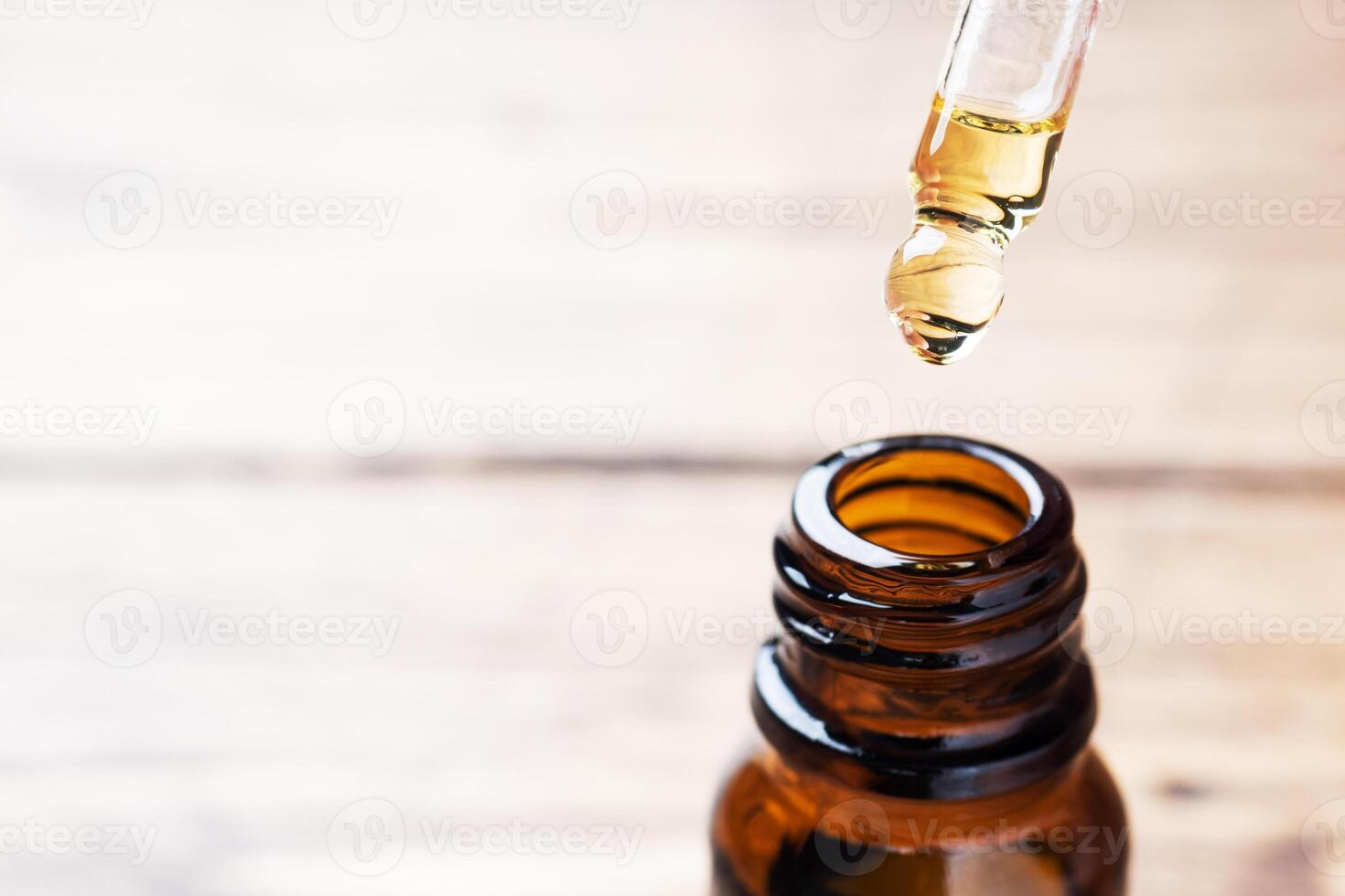 Drop falls from the pipette. Bottle of cosmetic oil with a pipette on a wooden background. Copy space. Selective focus. photo