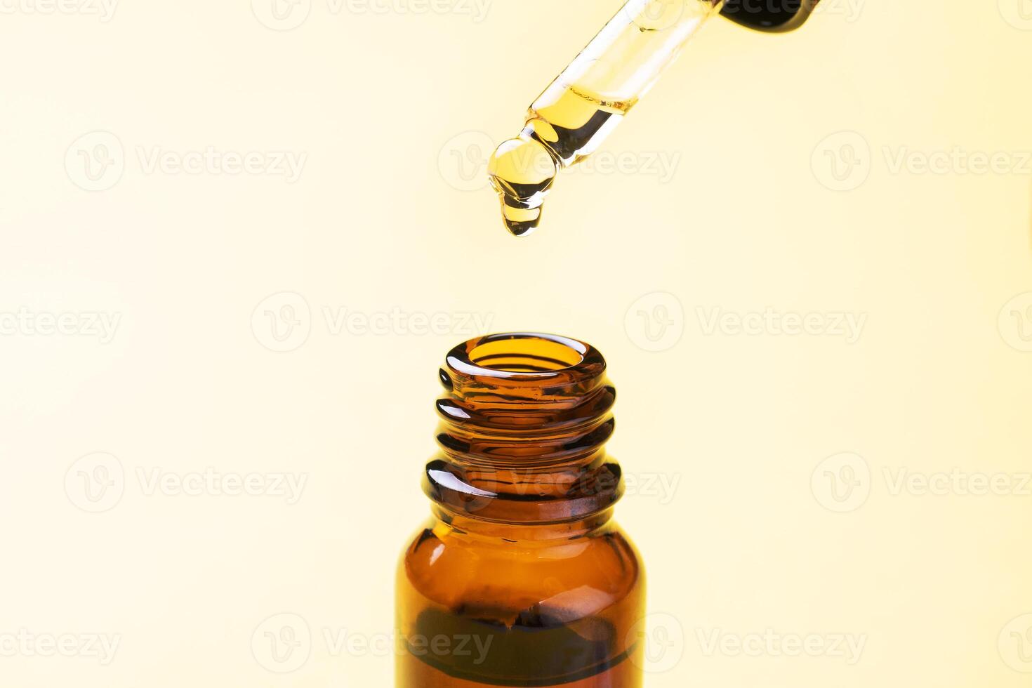 Drop falls from the pipette. Bottle of cosmetic oil with a pipette on a yellow background. Copy space. Selective focus. photo