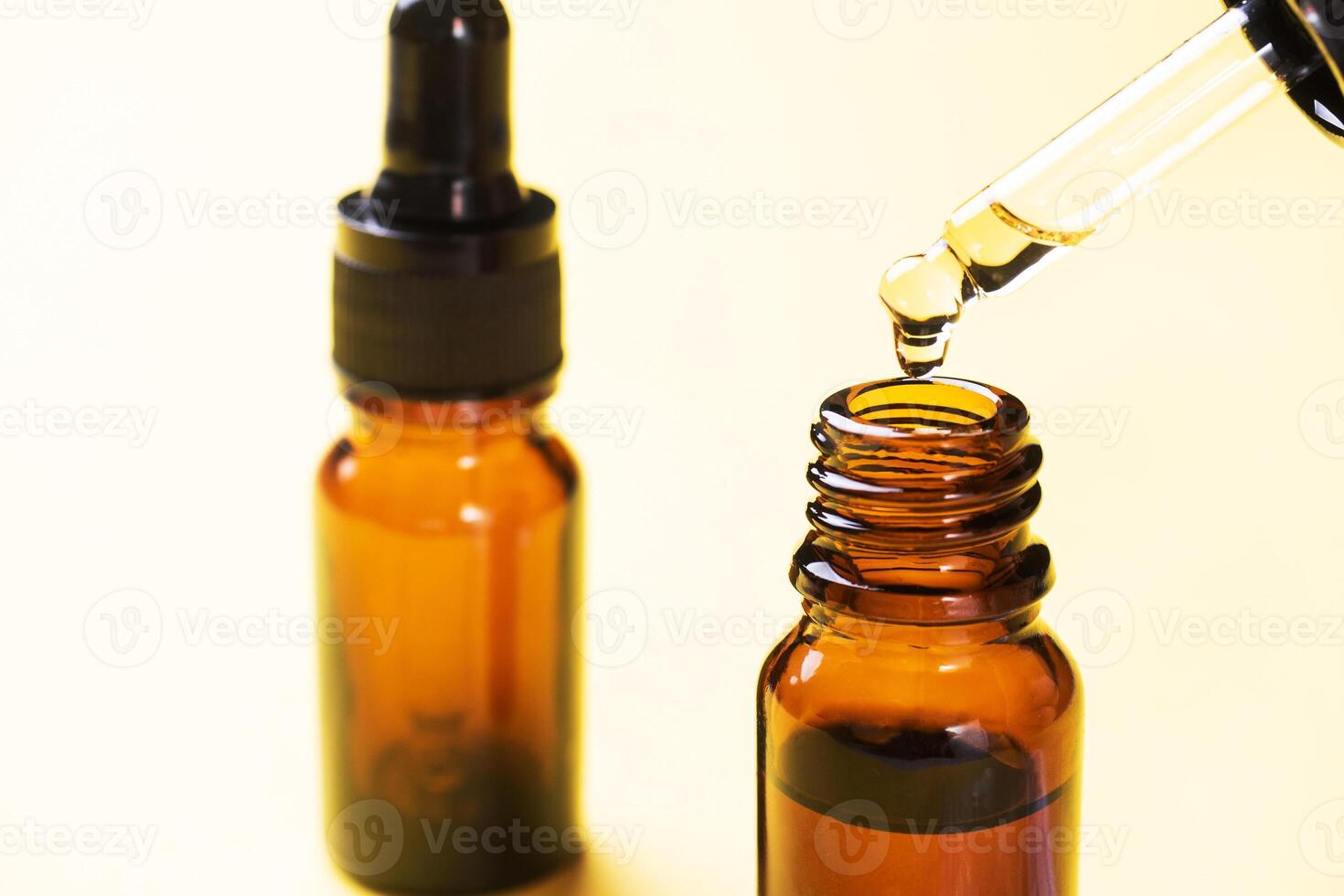 Drop falls from the pipette. Bottle of cosmetic oil with a pipette on a yellow background. Copy space. Selective focus. photo