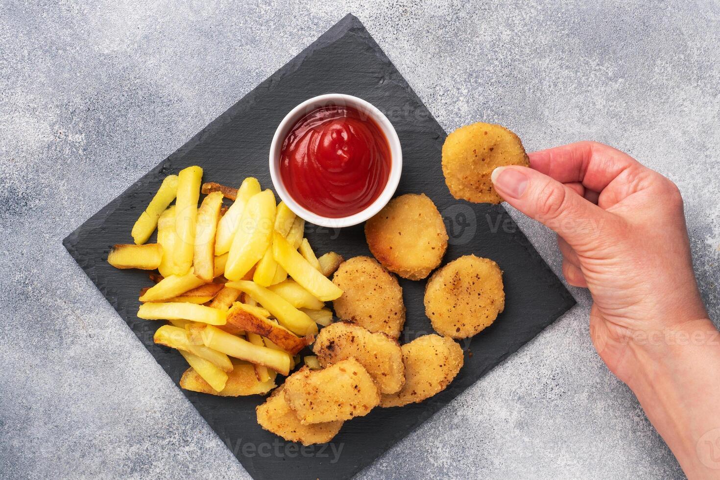 Fried potatoes and chicken nuggets with tomato ketchup sauce. Fast food concept of unhealthy food. Grey concrete table Copy space. photo