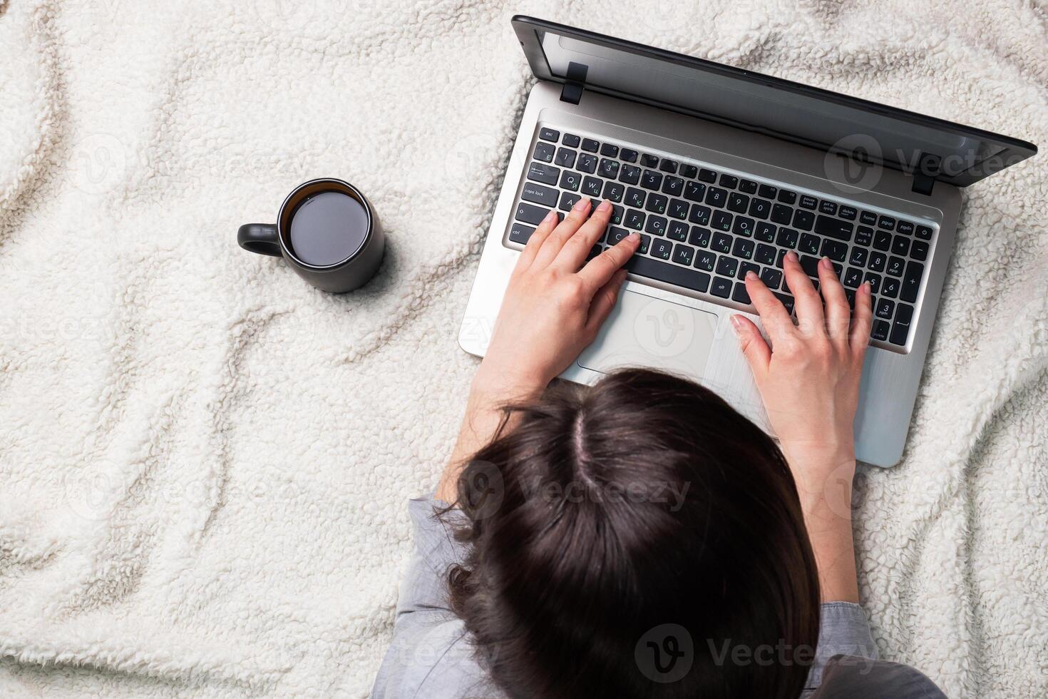 Woman lying on a white wool blanket and working at computer hands. Concept of working and learning at home. Copy space. photo