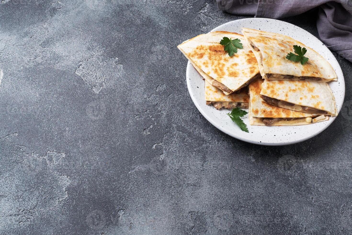 Pieces of quesadilla with mushrooms sour cream and cheese on a plate with parsley leaves. Concrete background copy space. photo
