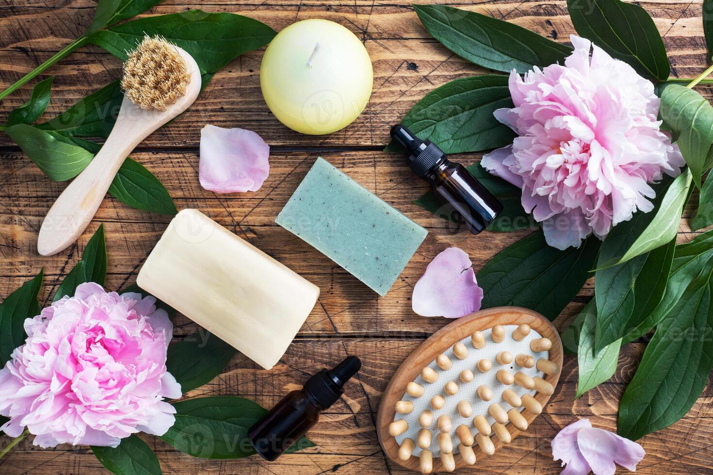 Concept SPA and Wellness. Massage brush, cosmetic oils and soap. Wooden background with peony flowers. photo