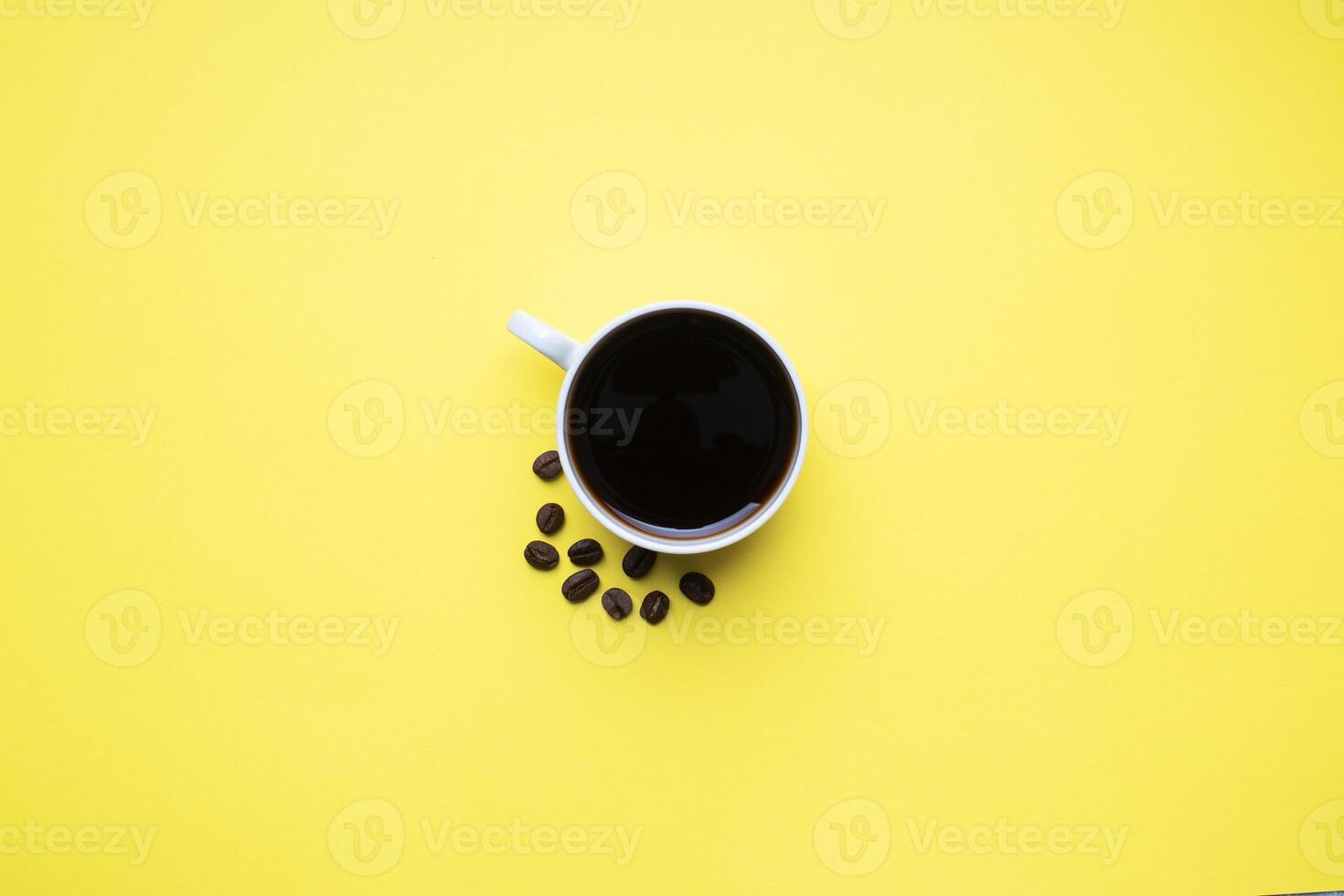 Black coffee in a Cup and coffee beans on a yellow background. Top view Copy space. photo