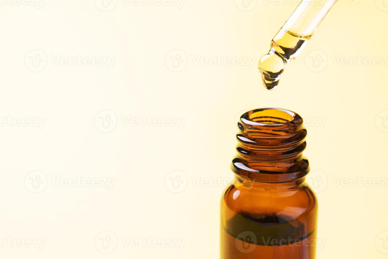 Drop falls from the pipette. Bottle of cosmetic oil with a pipette on a yellow background. Copy space. Selective focus. photo
