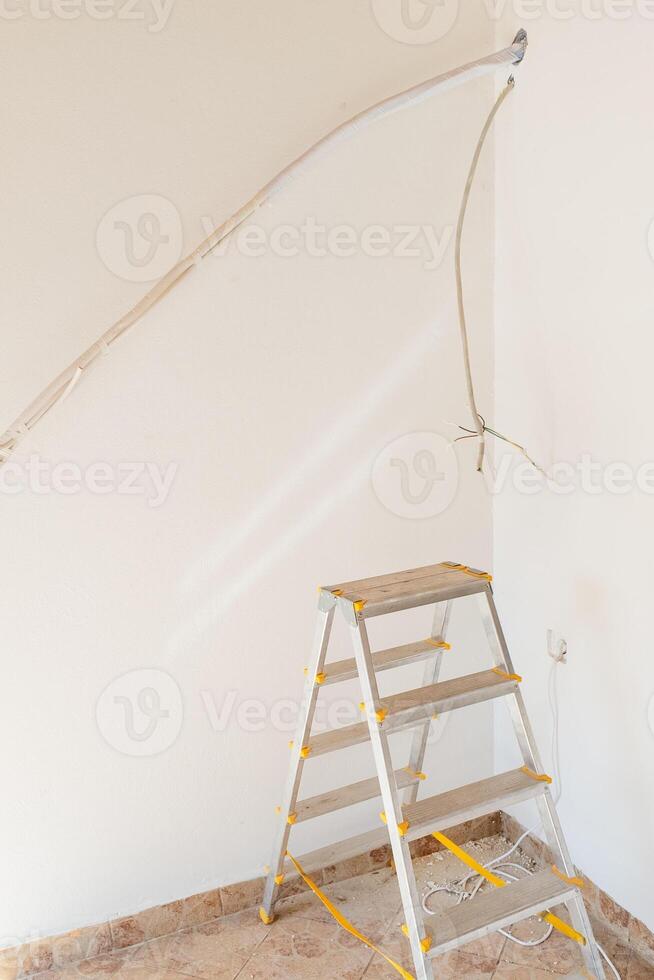A stepladder in a corner of a room under renovation shows exposed electrical wiring and partially painted walls, highlighting home improvement safety concerns photo