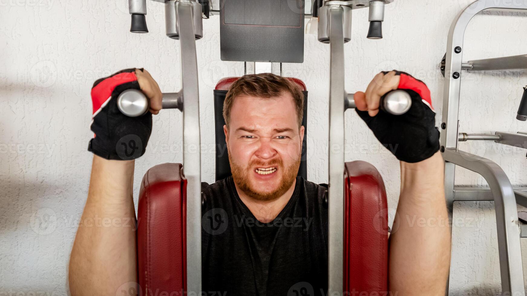 Caucasian man straining while using weight machine in the gym, focusing on fitness and physical challenge photo