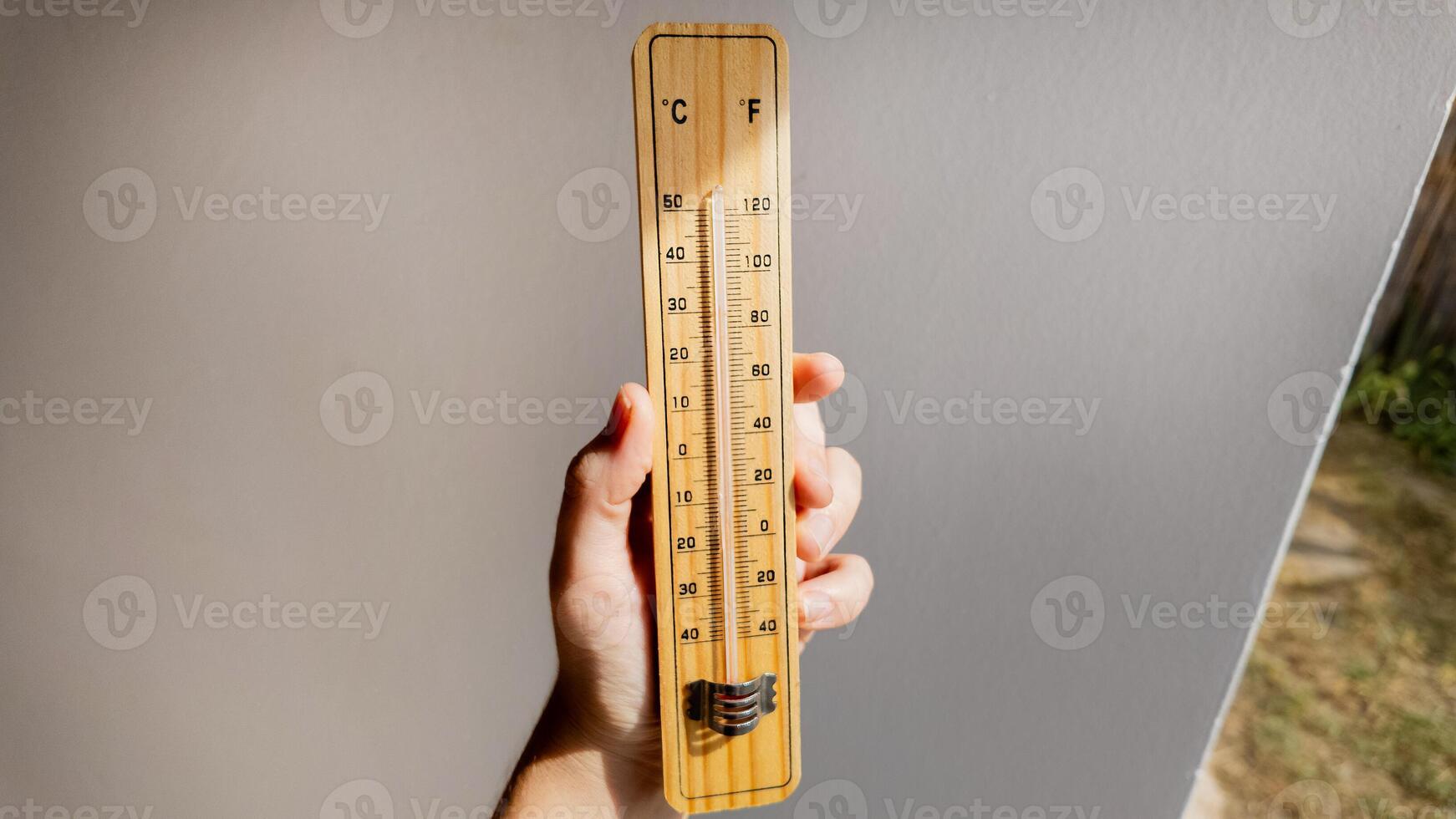 A hand holding a wooden thermometer indicates rising temperatures, highlighting concerns about global warming and climate change effects photo