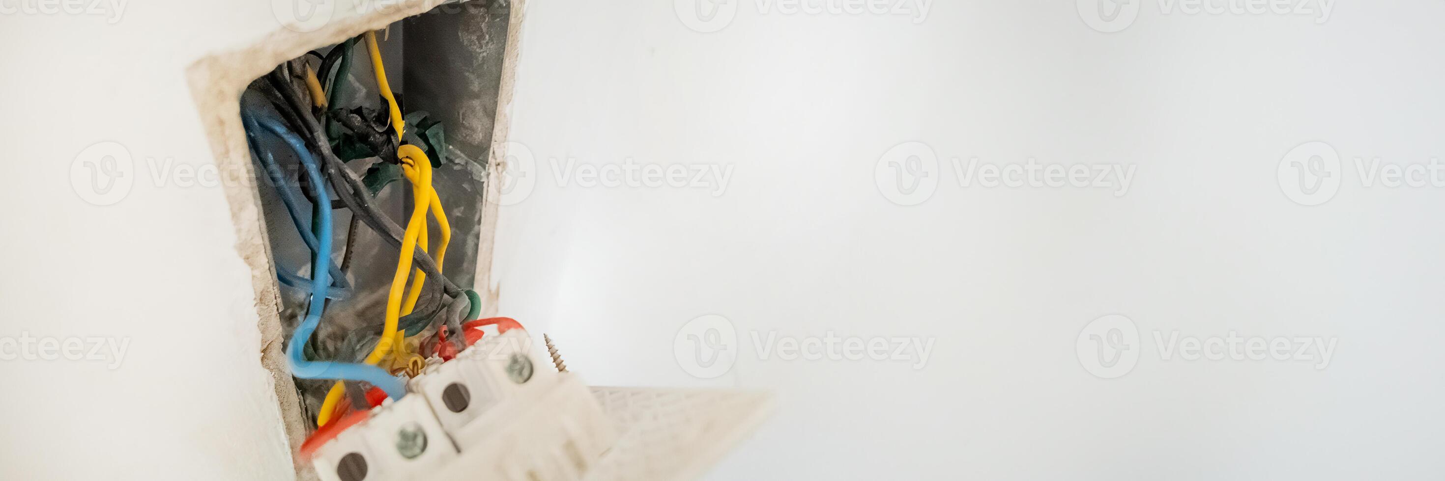 Close up of exposed electrical wiring in a wall socket, highlighting the risk of electrical hazards and DIY repair challenges photo